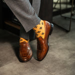 A light rust-orange men's dress sock with a bold black leaf motif