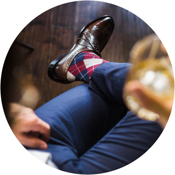 a man with his legs crossed wearing argyle men's dress socks, brown shoes, and navy suit