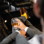 Man sitting, taking wine wearing honeycomb, solid, ribbed men's dress socks with brown shoes.