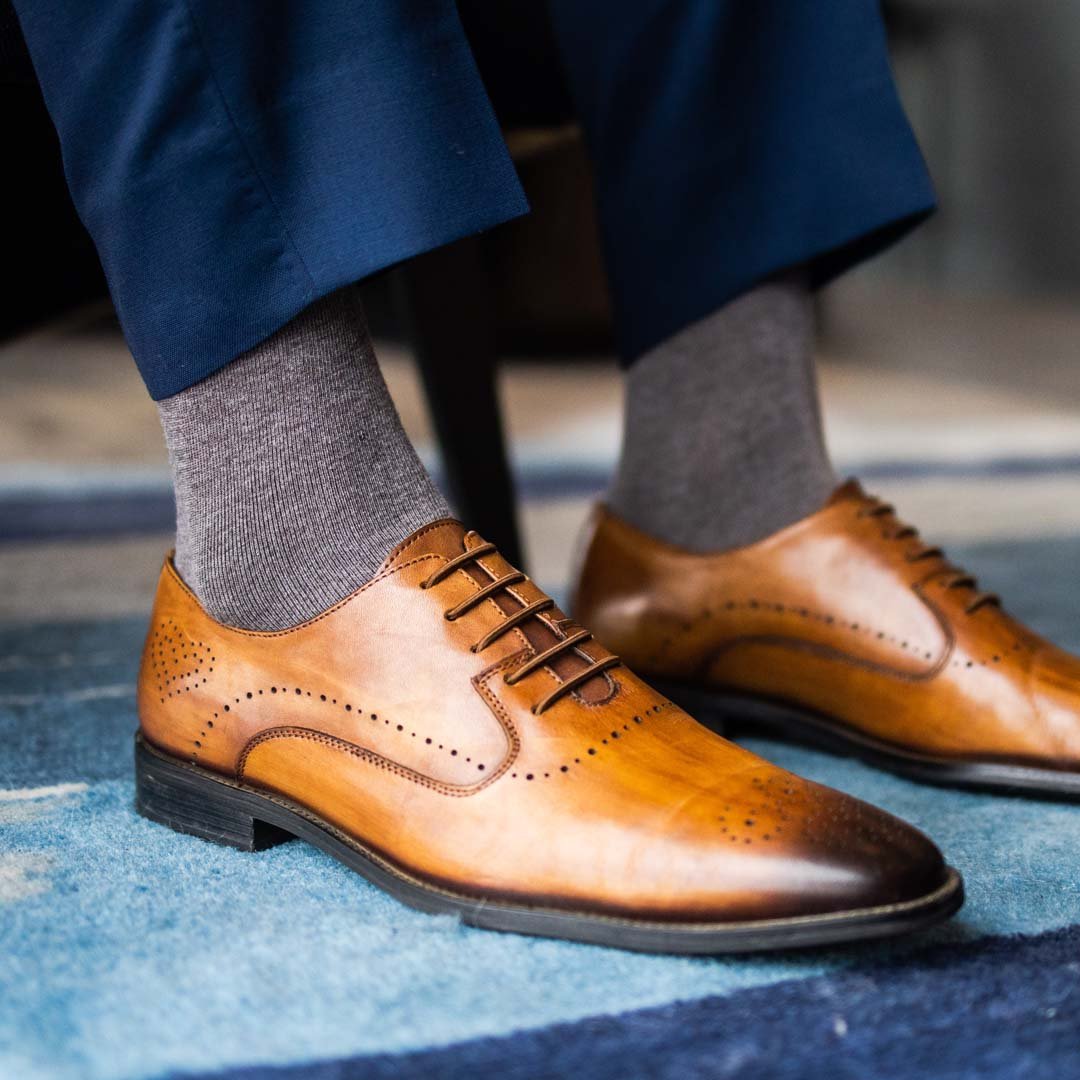 Man sitting wearing steel gray men's dress socks and brown shoes.
