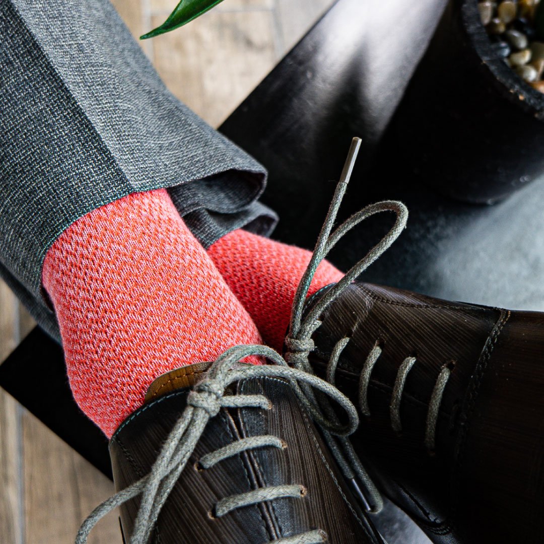 A man wearing A coral and salmon men's dress sock with a micro-chevron pattern with grey slacks and brown shoes