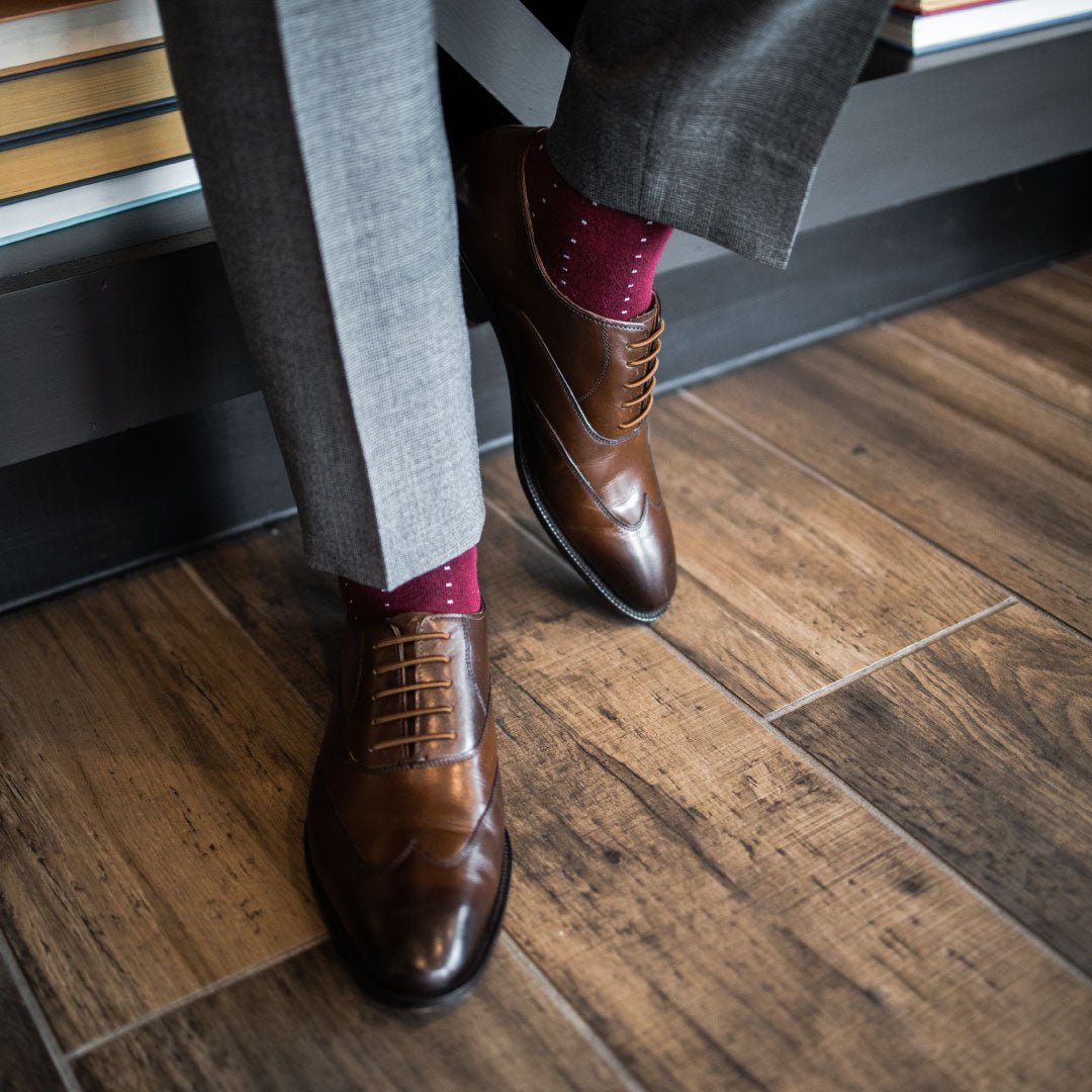Man wearing Deep red sock with light blue pin dots, brown shoes, and grey trousers