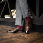 Man wearing Deep red sock with light blue pin dots, brown shoes, and gray trousers