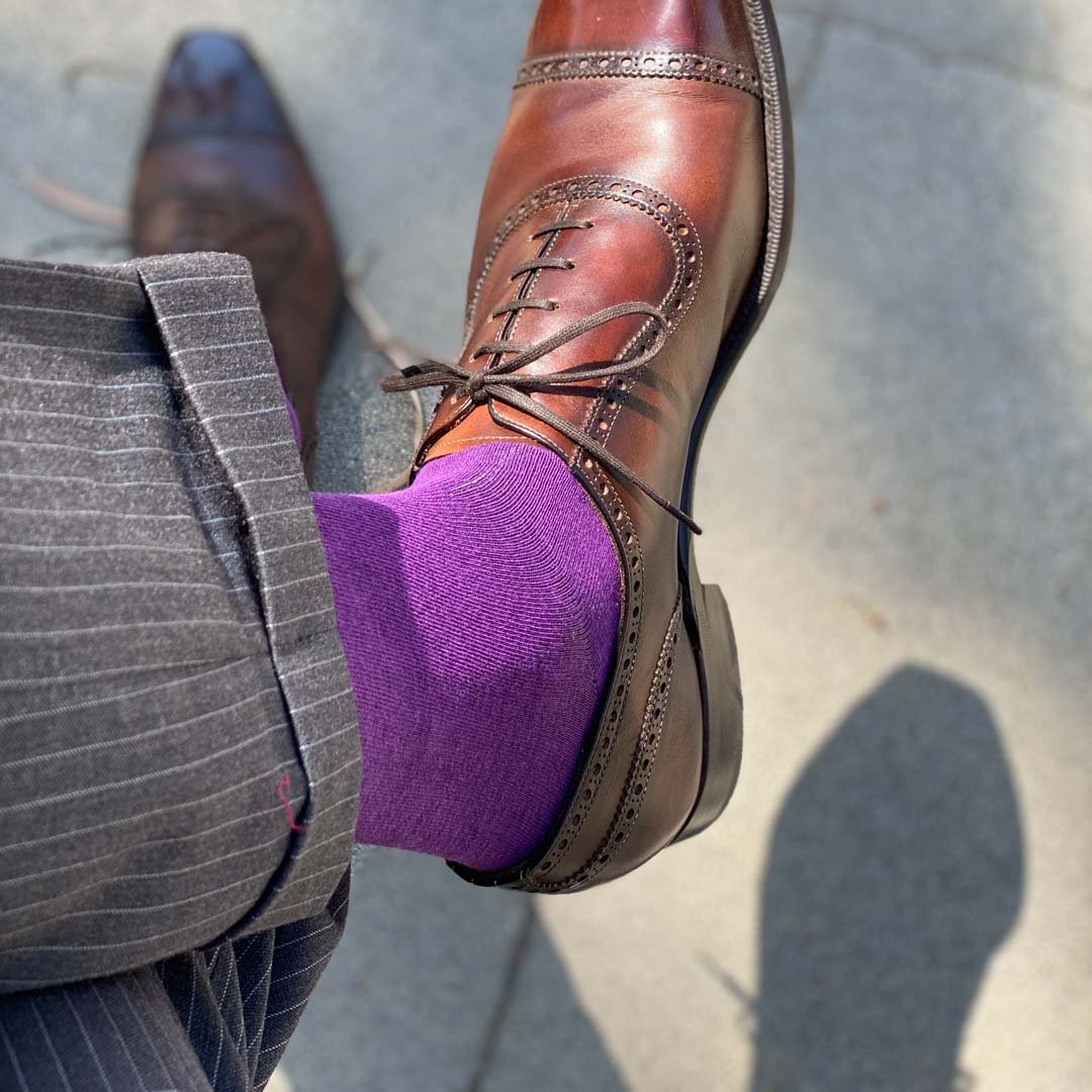 Man sitting with legs crossed wearing plum purple men's dress socks and shoes.