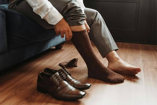 Man putting on brown dress socks beside leather dress shoes.