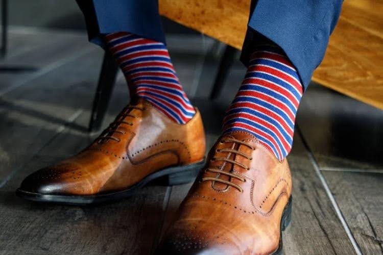 Brown dress shoes with striped socks and a navy suit.