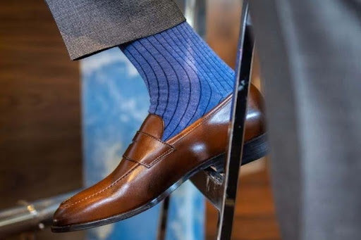 Brown leather loafers with blue striped dress socks and grey trousers.