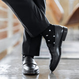 Model wearing black and grey micro-diamond dress socks with black trousers and black leather penny loafers, standing crossed-leg view.