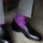 The Plum & Lavender Square-Grid dress socks with tailored trousers and loafers in a seated lounge view