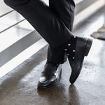 Model wearing black and grey micro-diamond dress socks with black trousers and black leather penny loafers, standing crossed-leg view.