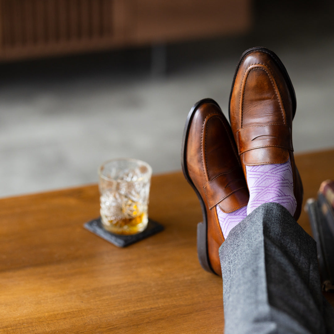 The Lavender & Plum Square-Grid dress socks with tailored trousers and loafers in a seated lounge view