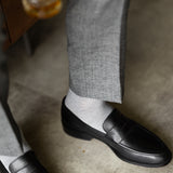 The Pearl Grey Square-Grid dress socks with tailored trousers and loafers in a seated lounge view