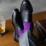 The Plum & Lavender Square-Grid dress socks with tailored trousers and loafers in a seated lounge view