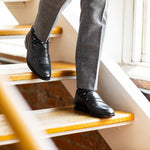 The Sage Green & Taupe Square-Grid dress socks with grey trousers and black dress shoes on warm loft stairs