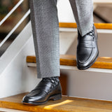 The Sage Green & Taupe Square-Grid dress socks with tailored trousers and loafers in a seated lounge view