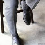 The Black & Silver Square-Grid dress sock with tailored trousers and a loafer in a seated foreground view