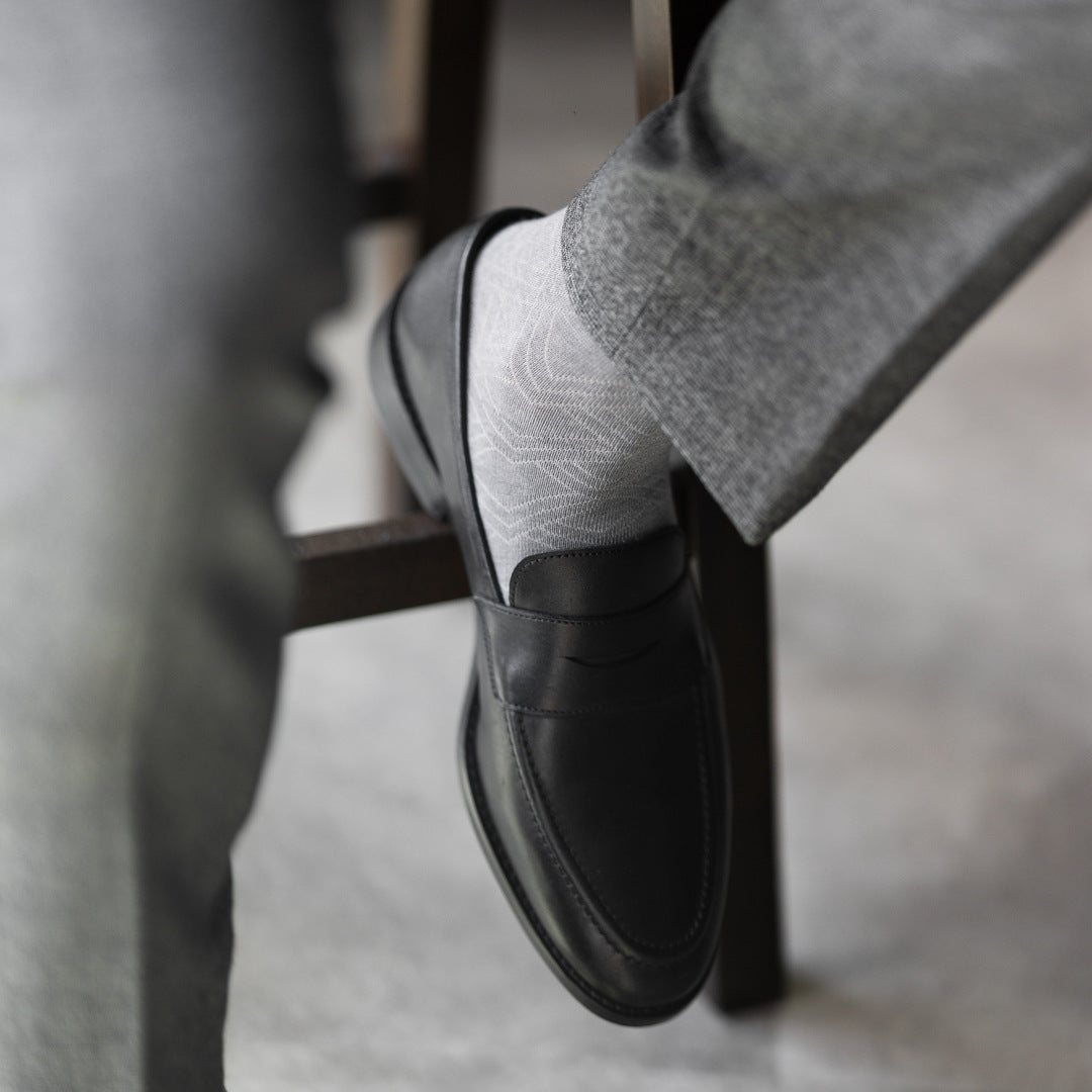 The Pearl Grey Square-Grid dress sock with tailored trousers and a loafer in a seated foreground view