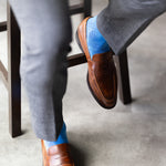 The Azure Blue & Cobalt Square-Grid dress sock with tailored trousers and a loafer in a seated foreground view