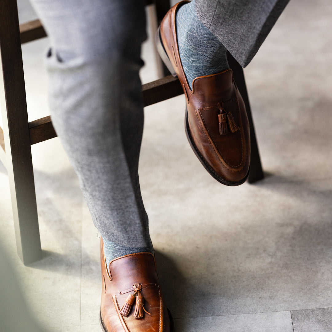 The Sage Green & Taupe Square-Grid dress sock with tailored trousers and a loafer in a seated foreground view