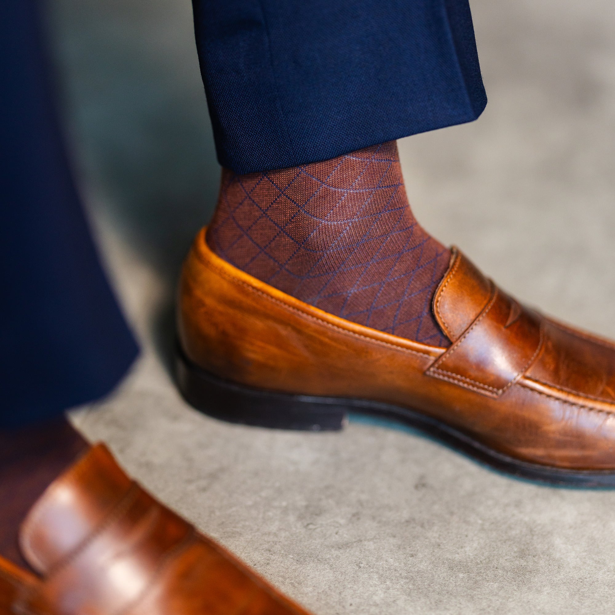 Close-up of a brown patterned dress sock with navy trousers and a brown loafer