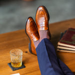 Brown patterned dress socks with navy trousers and loafers beside a glass