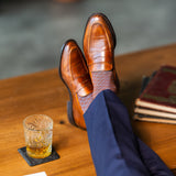 Brown patterned dress socks with navy trousers and loafers beside a glass