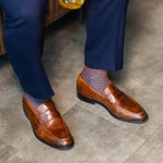 Brown patterned dress socks with navy trousers and brown penny loafers while standing