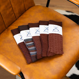 Five folded brown patterned dress socks arranged on a caramel leather chair
