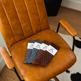 Four folded Gemstones dress socks arranged on a caramel leather chair