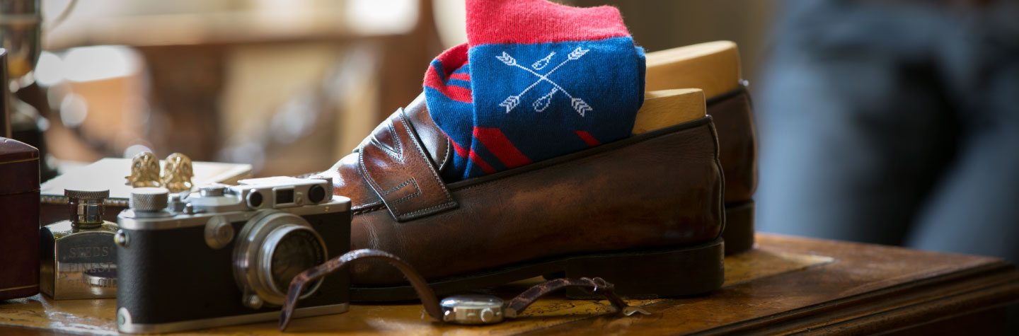 A pair of patterned men's dress socks inside a pair of penny loafers on top of a desk