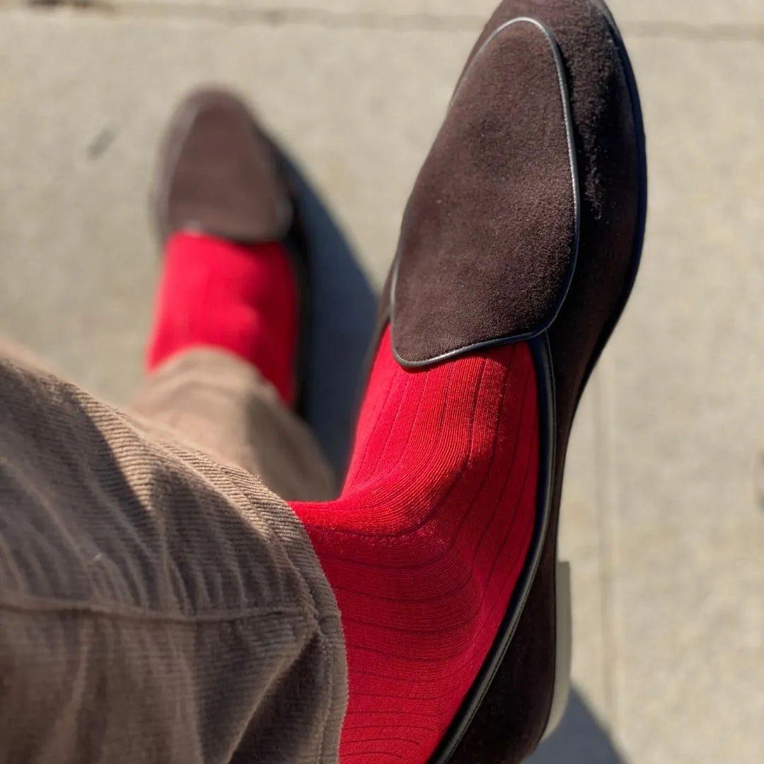 Man sitting with legs crossed wearing rose red ribbed men's dress socks.