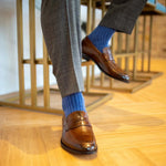 Man sitting wearing solid, blue, and navy blue ribbed men's dress socks and brown shoes.