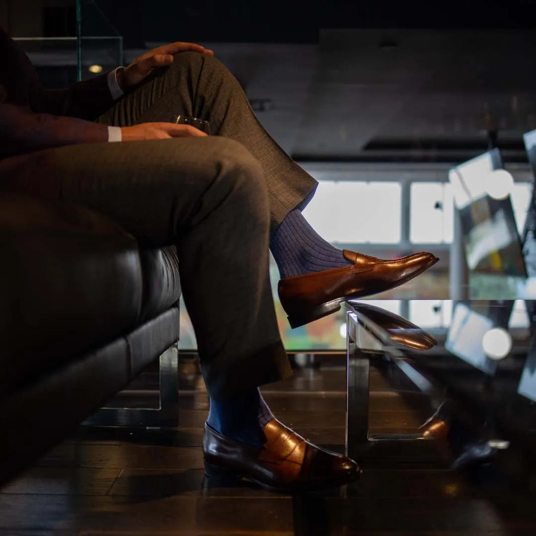 Man wearing solid, blue, and navy blue ribbed men's dress socks and brown shoes.