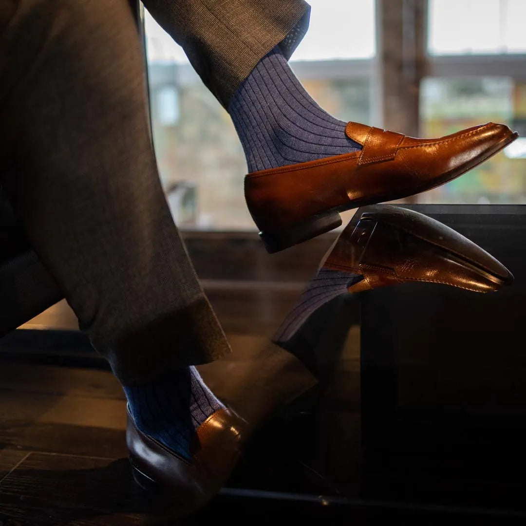 Man sitting wearing solid, blue, and navy blue ribbed men's dress socks and brown shoes.