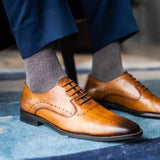 Man sitting wearing steel gray men's dress socks and brown shoes.