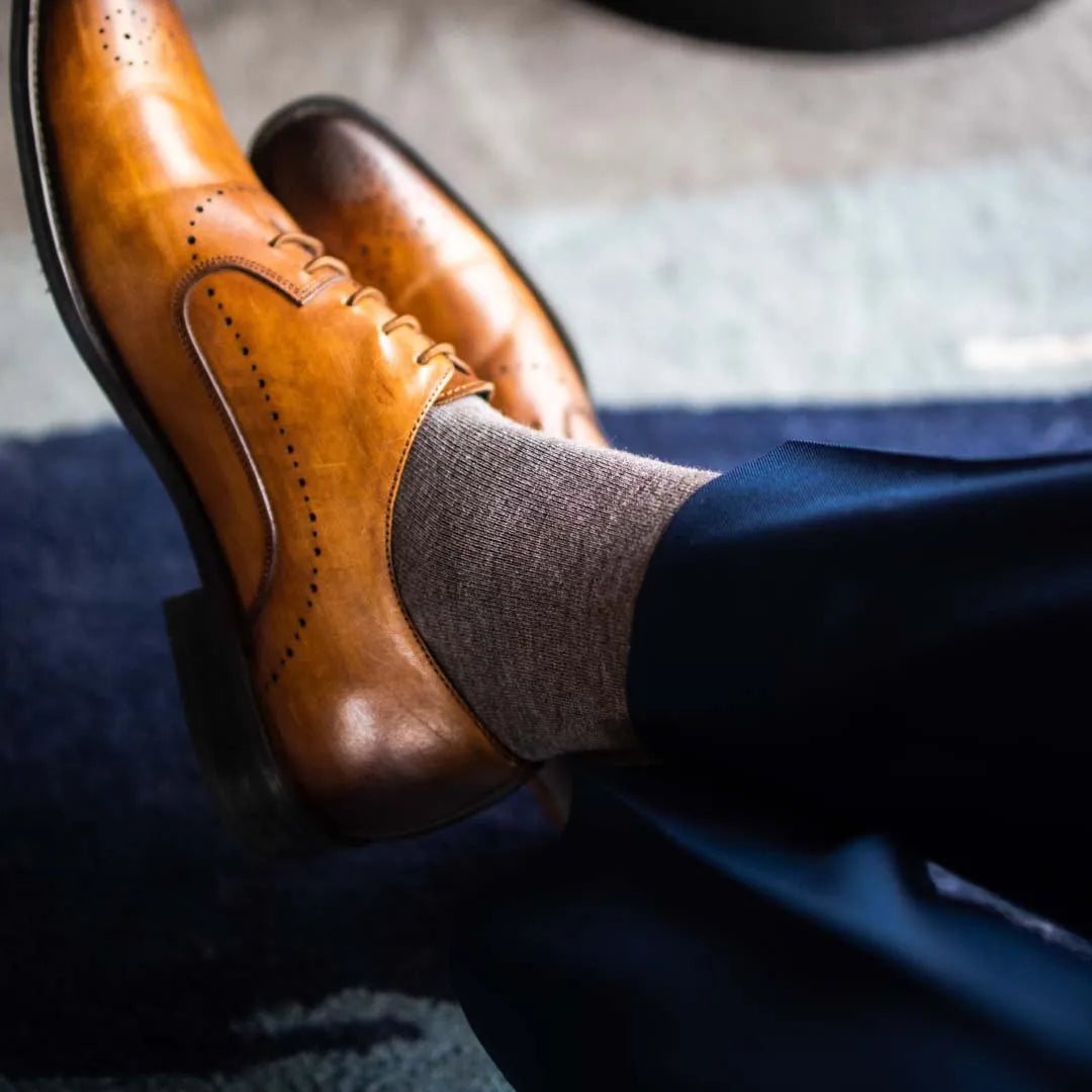 Man sitting wearing steel gray men's dress socks and brown shoes.