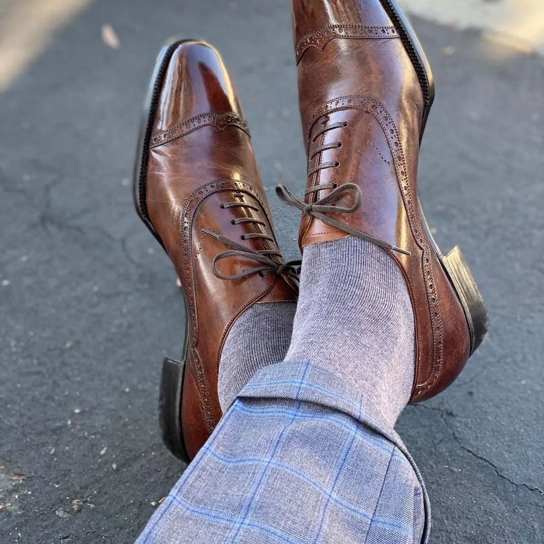 Man sitting down with legs crossed wearing steel gray men's dress socks and brown shoes.
