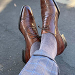 Man sitting down with legs crossed wearing steel gray men's dress socks and brown shoes.