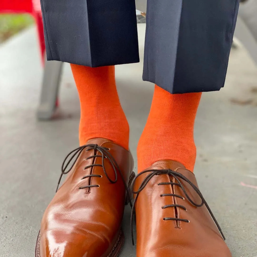 Man standing wearing navy blue pants, tangerine socks, and brown men's dress shoes.