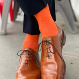 Man standing with feet crossed wearing navy blue pants, tangerine men's dress socks, and brown shoes.