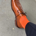 Man wearing navy blue pants, tangerine men's dress sock, and brown shoe.