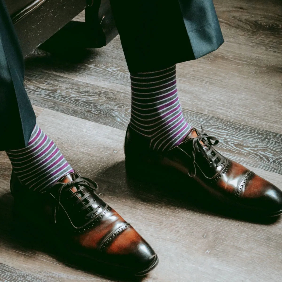 Guy sitting down wearing purple, grey, and white striped men's dress socks