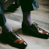 Guy sitting down wearing purple, grey, and white striped men's dress socks