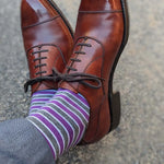 Man wearing purple, grey, and white striped dress socks and brown dress shoes