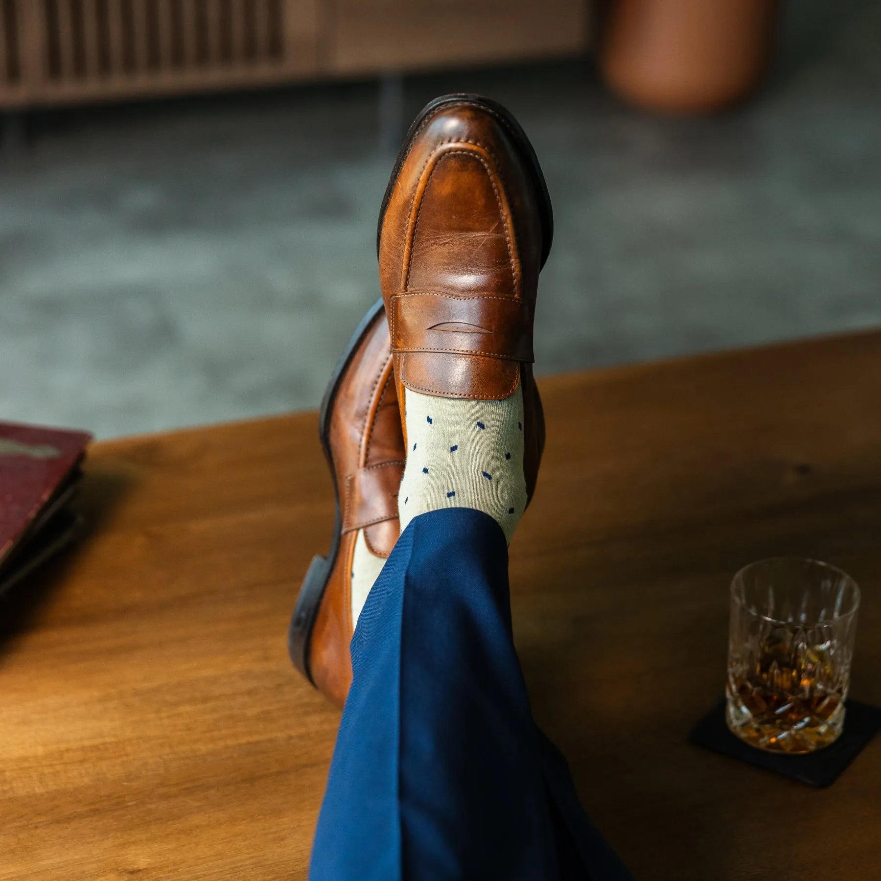 Men's dress socks with a crisp ivory base and deep navy micro-tile pattern, worn with navy slacks and brown leather loafers.