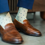 Men's dress socks with a crisp ivory base and deep navy micro-tile pattern, worn with navy slacks and brown leather loafers.