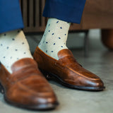 Men's dress socks with a crisp ivory base and deep navy micro-tile pattern, worn with navy slacks and brown leather loafers.