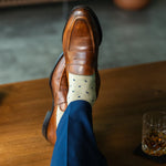 Men's dress socks with a crisp ivory base and deep navy micro-tile pattern, worn with navy slacks and brown leather loafers.
