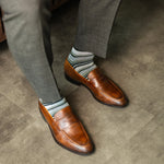 Brown loafers, gray pants, and striped socks on a concrete floor.