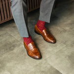 Person wearing brown shoes and red patterned socks on a concrete floor.